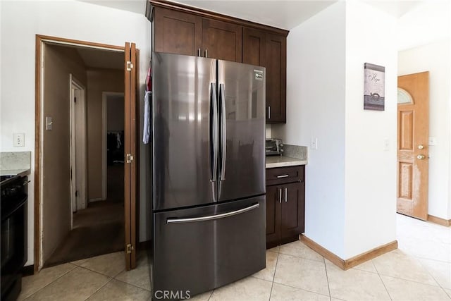 kitchen with freestanding refrigerator, range, light countertops, dark brown cabinets, and light tile patterned floors