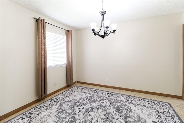 empty room featuring a chandelier, light tile patterned floors, and baseboards