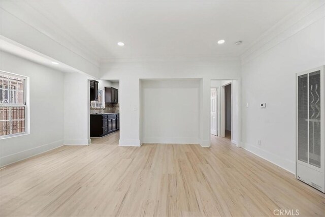 unfurnished living room with a heating unit, light wood finished floors, baseboards, crown molding, and recessed lighting