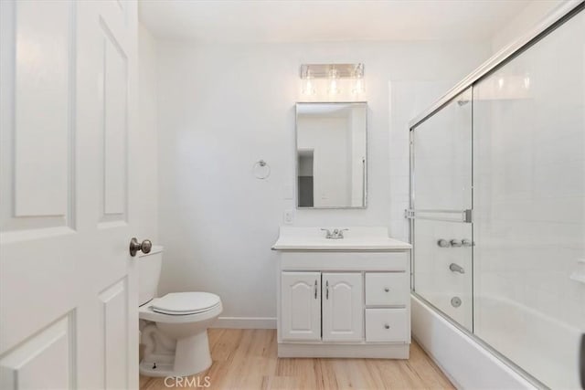 full bathroom with toilet, wood finished floors, vanity, bath / shower combo with glass door, and baseboards