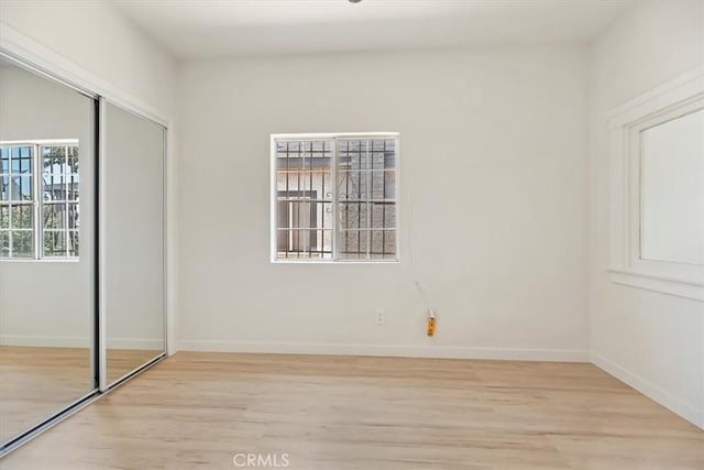 unfurnished bedroom featuring light wood-type flooring, a closet, and baseboards