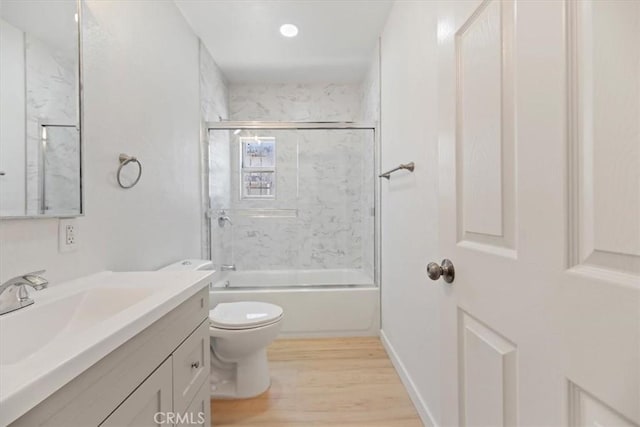 full bath with toilet, wood finished floors, vanity, and bath / shower combo with glass door