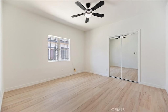 unfurnished bedroom featuring wood finished floors, a closet, baseboards, and a ceiling fan