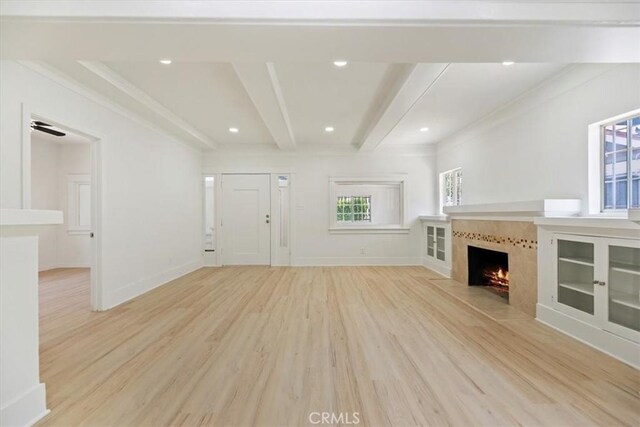 unfurnished living room with light wood-type flooring, healthy amount of natural light, a fireplace with flush hearth, baseboards, and beamed ceiling
