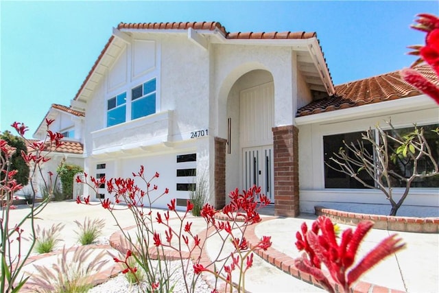 mediterranean / spanish-style house featuring a tiled roof, stucco siding, an attached garage, and brick siding