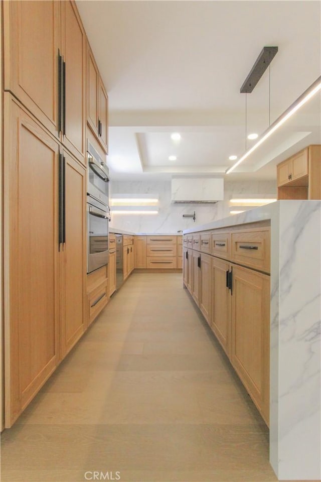 kitchen with a raised ceiling, light brown cabinetry, light wood-type flooring, recessed lighting, and light stone countertops