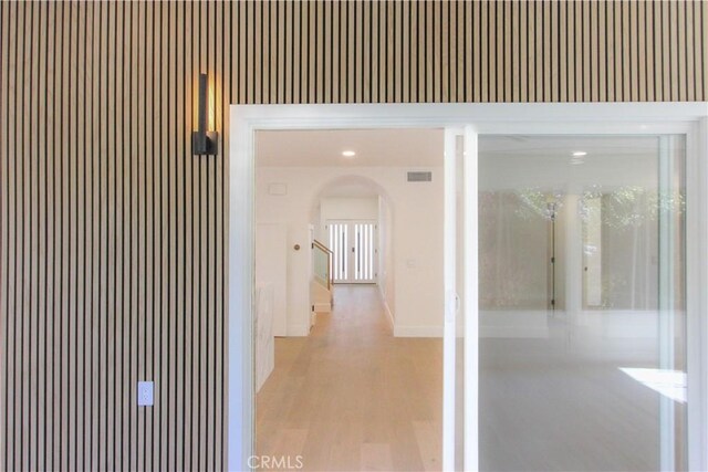 hallway featuring arched walkways, light wood-style flooring, and baseboards