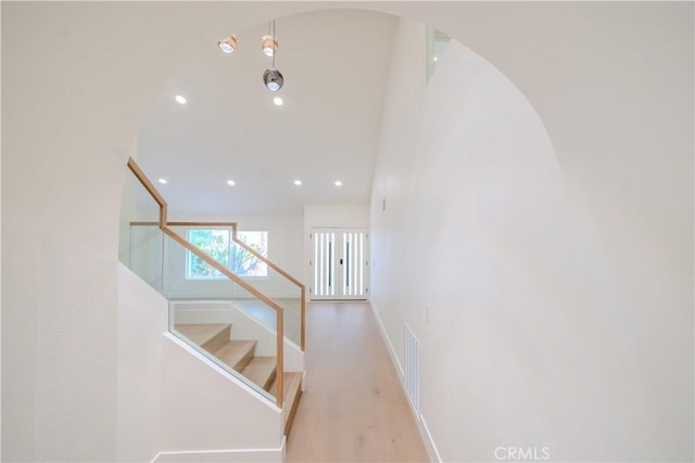 hallway featuring arched walkways, recessed lighting, stairway, wood finished floors, and baseboards