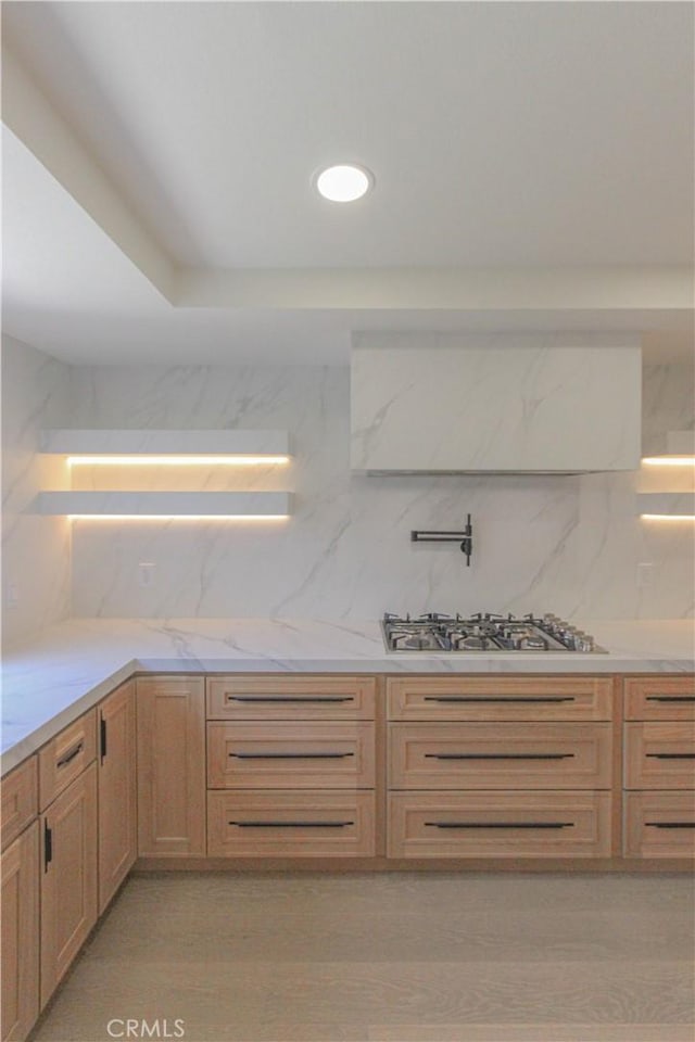 kitchen with stainless steel gas stovetop, decorative backsplash, light stone countertops, and light brown cabinets
