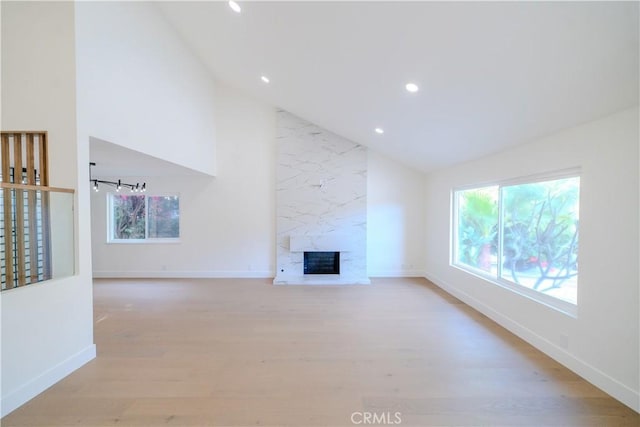 unfurnished living room featuring plenty of natural light, light wood finished floors, baseboards, recessed lighting, and a premium fireplace