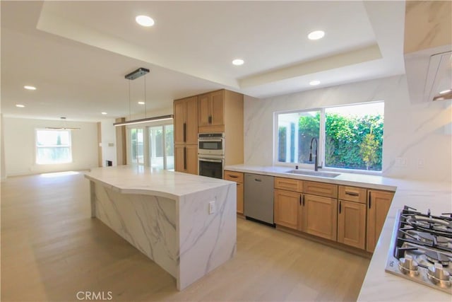 kitchen featuring appliances with stainless steel finishes, a sink, light stone countertops, light wood finished floors, and decorative light fixtures