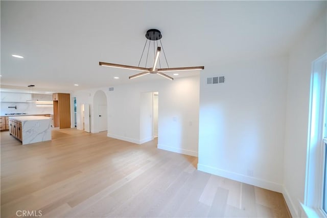 unfurnished living room featuring arched walkways, recessed lighting, light wood-style floors, and baseboards