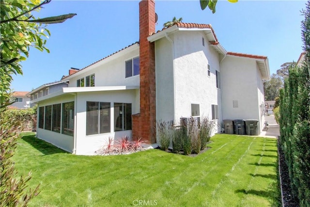 back of house with a chimney, stucco siding, a lawn, a sunroom, and a tiled roof