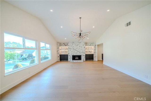 unfurnished living room with light wood finished floors, a chandelier, a fireplace, baseboards, and high vaulted ceiling