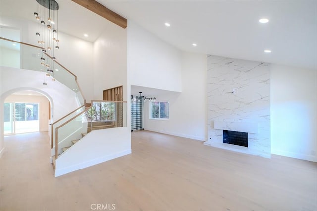 unfurnished living room featuring high vaulted ceiling, a fireplace, stairway, recessed lighting, and arched walkways