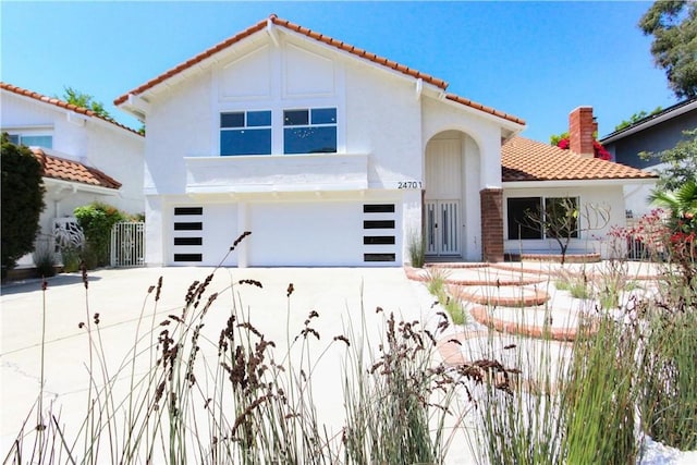 mediterranean / spanish-style house featuring an attached garage, a tile roof, stucco siding, and driveway