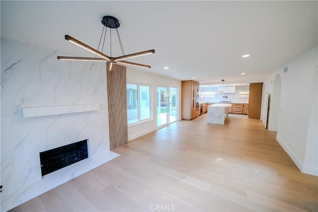unfurnished living room featuring a fireplace, light wood-style flooring, recessed lighting, arched walkways, and baseboards