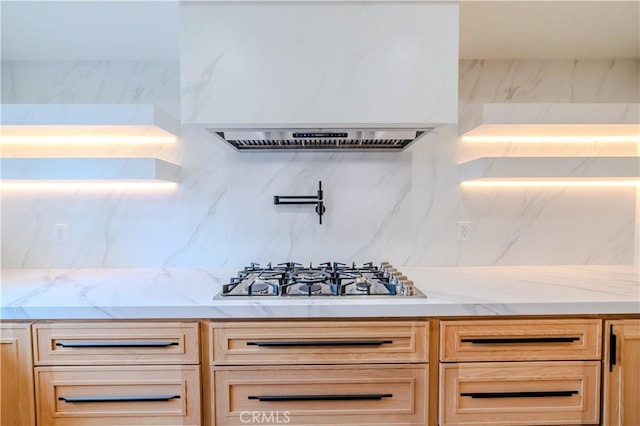 kitchen view of stainless steel gas cooktop, pot filler, tasteful backsplash, light stone countertops, and exhaust hood
