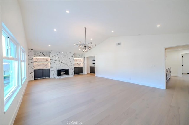 unfurnished living room featuring a chandelier, vaulted ceiling, a premium fireplace, light wood-style flooring, and recessed lighting
