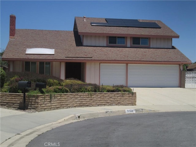 11133 Shetland Ave, Montclair, CA 91763 - view of front of home with board and batten siding, roof mounted solar panels, an attached garage, driveway, and roof with shingles