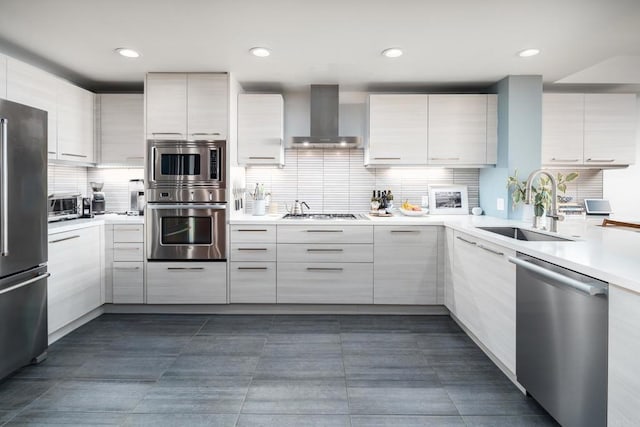 kitchen with appliances with stainless steel finishes, wall chimney range hood, a sink, modern cabinets, and recessed lighting