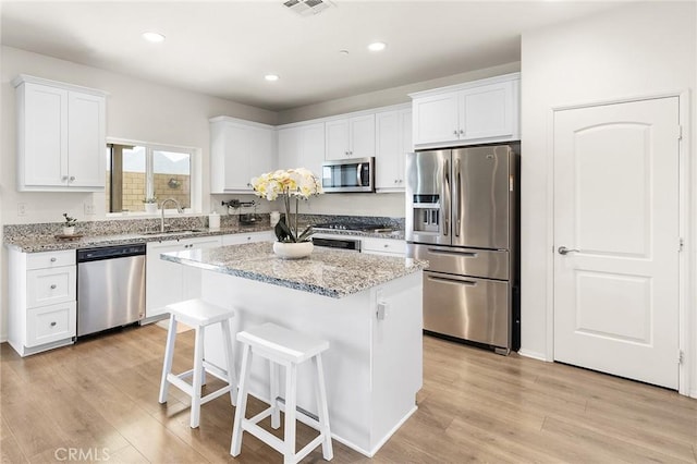 29628 Dotted Mint, Winchester, CA 92596 - kitchen with stainless steel appliances, a sink, a kitchen bar, white cabinetry, and light wood finished floors