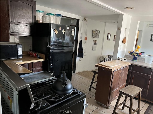 kitchen featuring black appliances, light tile patterned floors, backsplash, and dark brown cabinets