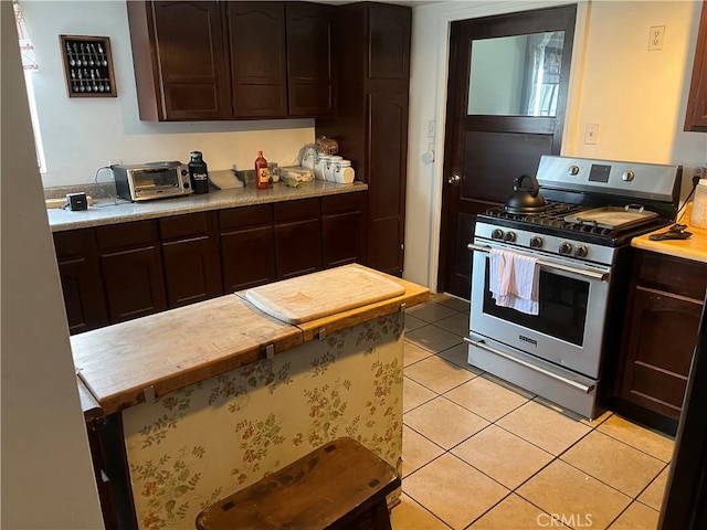 kitchen with stainless steel gas range oven, light countertops, light tile patterned floors, and dark brown cabinetry