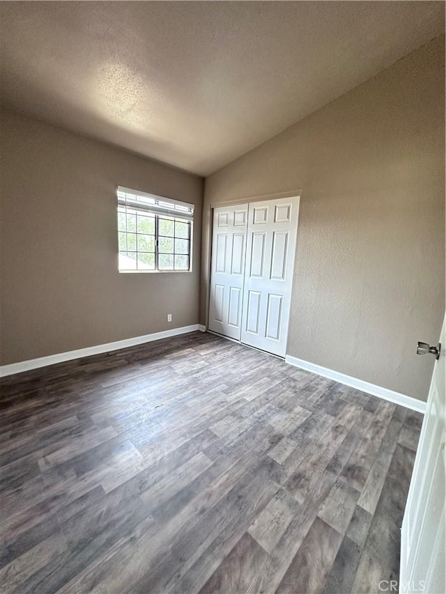unfurnished bedroom with dark wood-style floors, vaulted ceiling, baseboards, a closet, and a textured ceiling