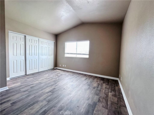 unfurnished bedroom featuring wood finished floors, baseboards, vaulted ceiling, and a closet