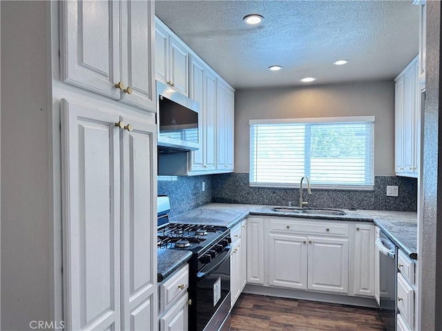 kitchen with stainless steel appliances, a sink, a textured ceiling, white cabinetry, and dark wood-style floors