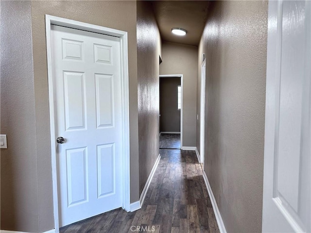 corridor with dark wood finished floors, a textured wall, and baseboards