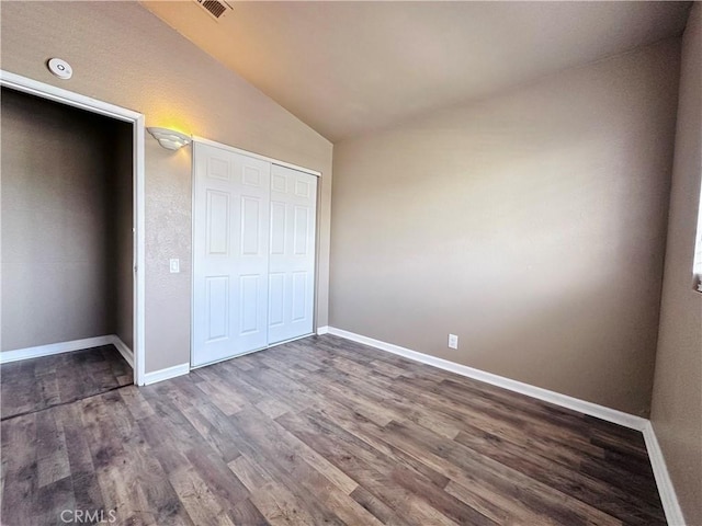 unfurnished bedroom featuring vaulted ceiling, dark wood finished floors, baseboards, and a closet