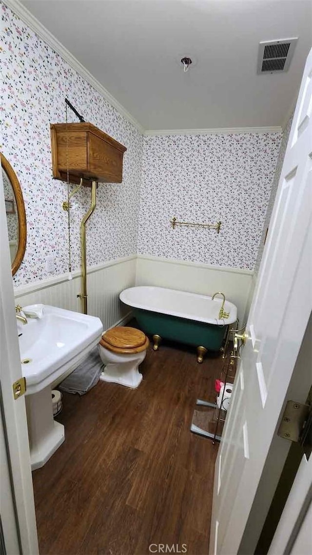 bathroom with wainscoting, wallpapered walls, a freestanding bath, wood finished floors, and crown molding