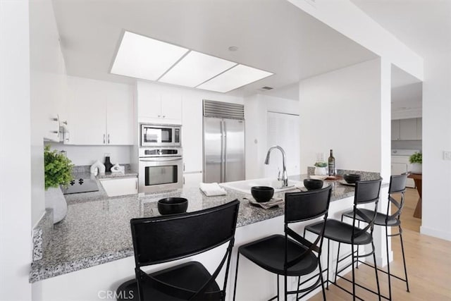 850 E Ocean Blvd Unit 602, Long Beach, CA 90802 - kitchen with built in appliances, a peninsula, white cabinets, light wood-style flooring, and a kitchen breakfast bar