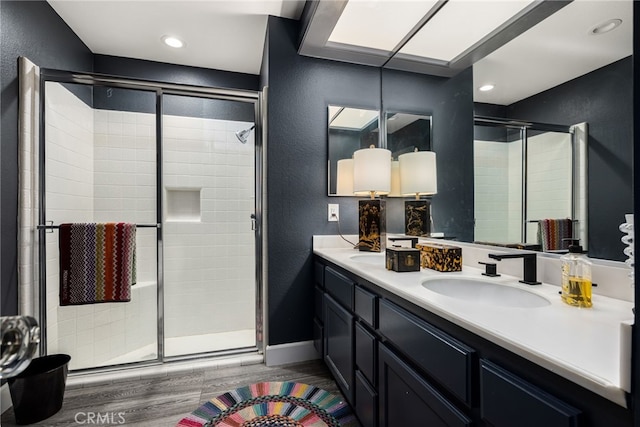 bathroom with wood finished floors, a stall shower, a textured wall, double vanity, and recessed lighting