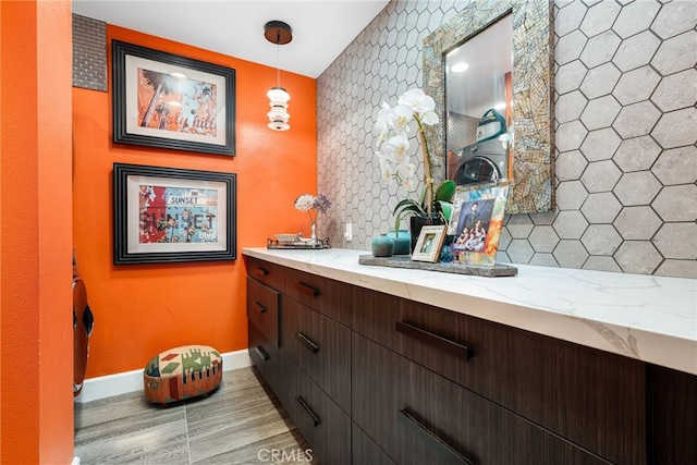 bathroom featuring baseboards, backsplash, vanity, an accent wall, and wood finished floors