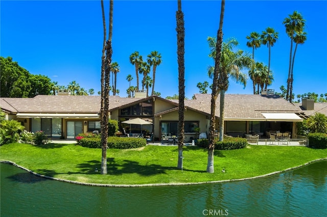 back of property featuring a water view, a lawn, and a patio area
