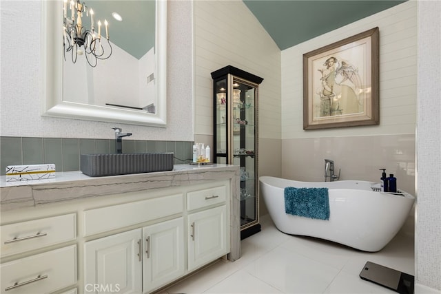 bathroom with a freestanding tub, vanity, vaulted ceiling, tile patterned flooring, and a chandelier