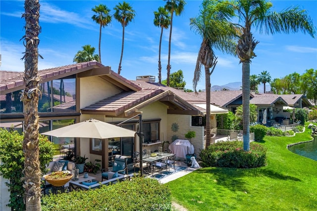 rear view of house featuring a lawn, stucco siding, a patio area, and a tiled roof