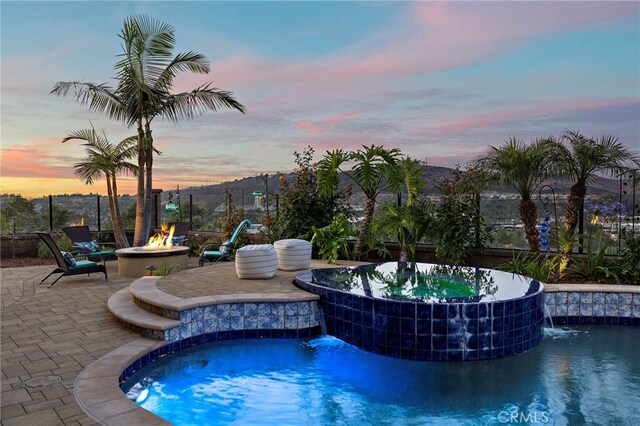 7051 Sitio Caliente, Carlsbad, CA 92009 - pool at dusk featuring a pool with connected hot tub, an outdoor fire pit, and a patio area