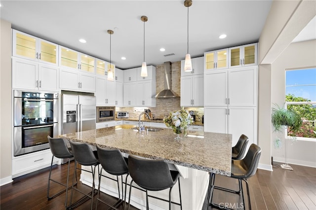 7051 Sitio Caliente, Carlsbad, CA 92009 - kitchen featuring appliances with stainless steel finishes, wall chimney range hood, backsplash, dark wood finished floors, and white cabinets
