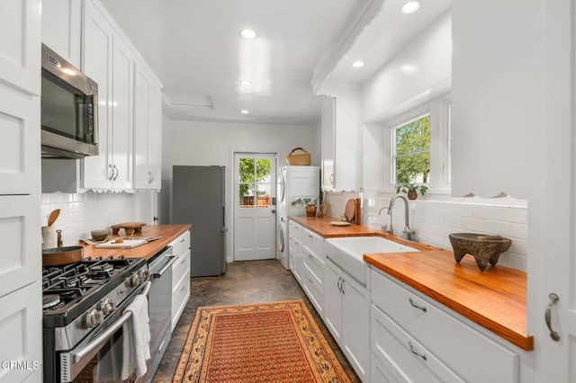 kitchen with appliances with stainless steel finishes, a sink, butcher block countertops, healthy amount of natural light, and recessed lighting