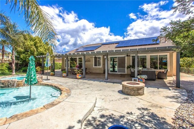 back of property with roof mounted solar panels, a pergola, an outdoor living space with a fire pit, stucco siding, and a patio area