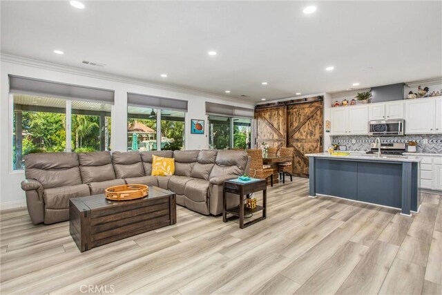 living area with a barn door, crown molding, recessed lighting, and light wood-type flooring