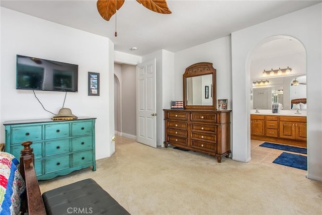 bedroom featuring arched walkways, light carpet, ensuite bathroom, a ceiling fan, and a sink