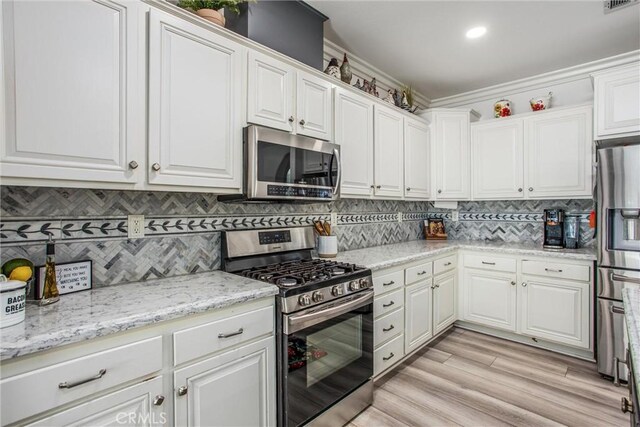 kitchen featuring appliances with stainless steel finishes, white cabinetry, decorative backsplash, light wood-style floors, and recessed lighting