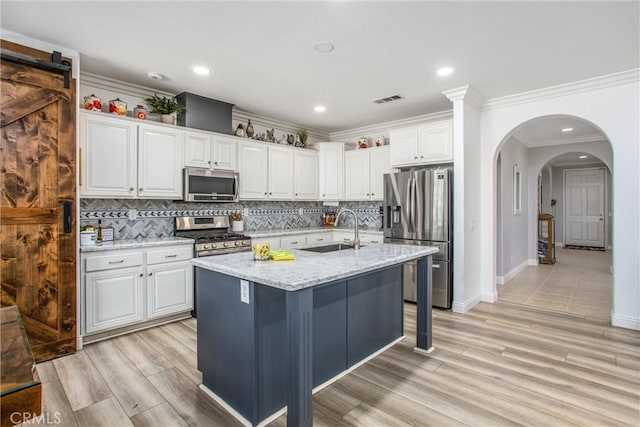 kitchen featuring appliances with stainless steel finishes, a sink, white cabinetry, tasteful backsplash, and ornamental molding
