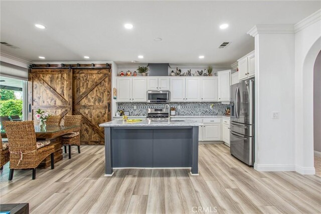 kitchen with stainless steel appliances, arched walkways, light wood-type flooring, crown molding, and white cabinetry