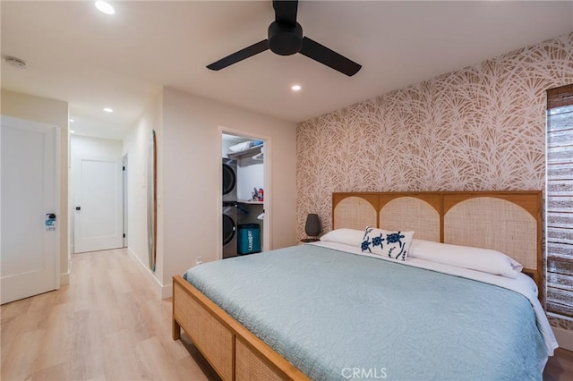 bedroom featuring wallpapered walls, stacked washer / drying machine, light wood-style floors, recessed lighting, and a walk in closet